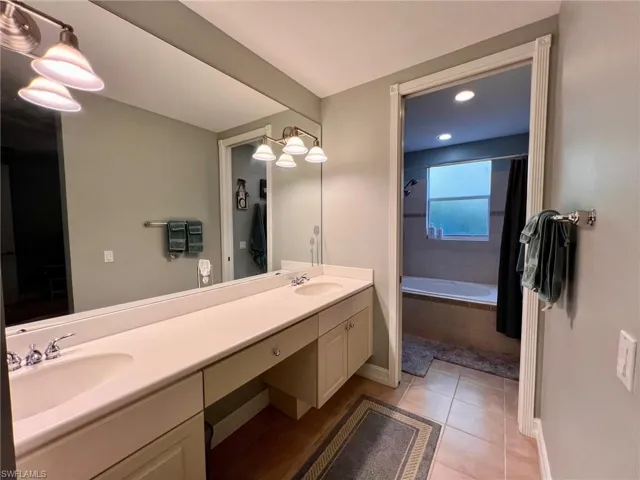Bathroom with double vanity, tiled shower / bath combo, and light tile patterned floors