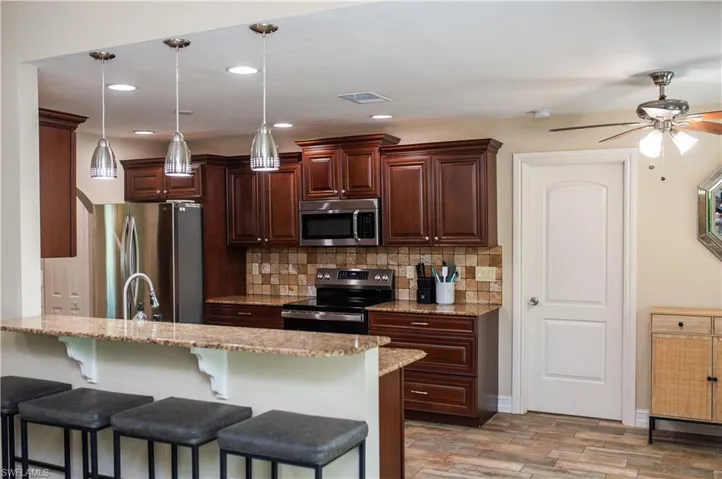 Kitchen featuring granite countertops, appliances with stainless steel finishes, tasteful backsplash, and a breakfast bar.