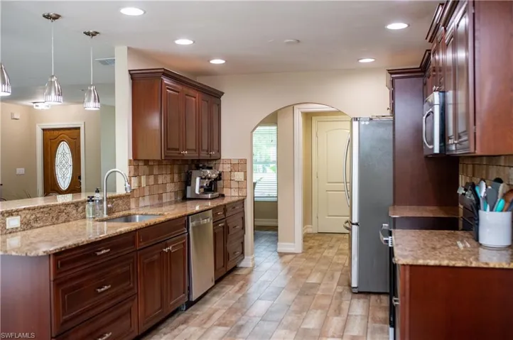 Kitchen with arched walkways, decorative backsplash, granite countertops, appliances with stainless steel finishes, and decorative light fixtures