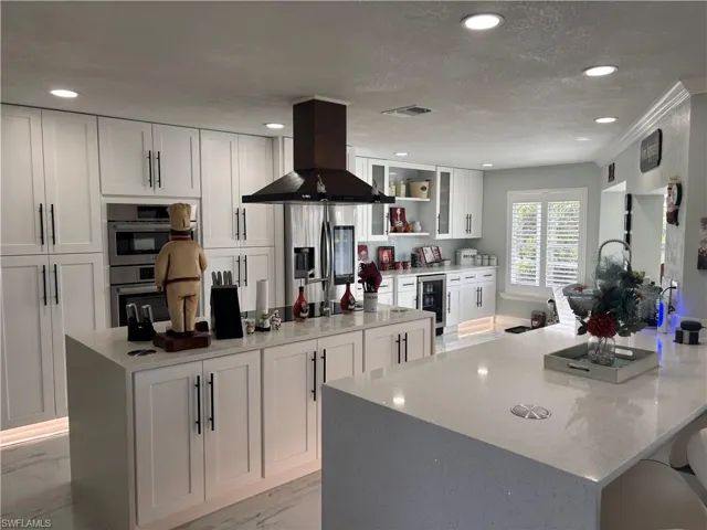 Kitchen featuring range hood, appliances with stainless steel finishes, wine cooler, white cabinets, and recessed lighting