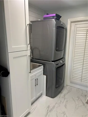 Laundry room with estacked washer and dryer, cabinet space, and light marble finish flooring