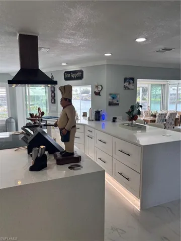 Kitchen featuring extractor fan, a textured ceiling, white cabinetry, ornamental molding, and plenty of natural light