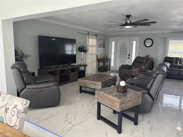 Living area featuring marble tiled flooring, a ceiling fan, a barn door, crown molding, and a textured ceiling