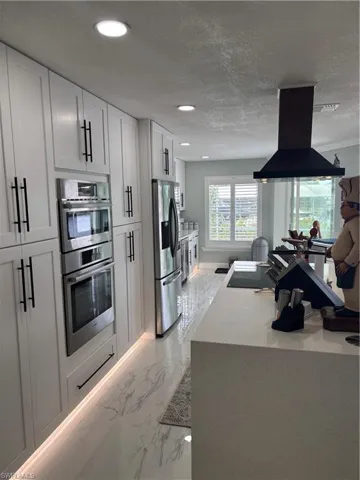 Kitchen featuring ventilation hood, fridge with ice dispenser, double oven, light marble finish flooring, and recessed lighting