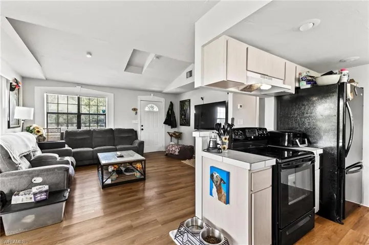 Kitchen with black appliances, tile countertops, hardwood / wood-style floors, and vaulted ceiling