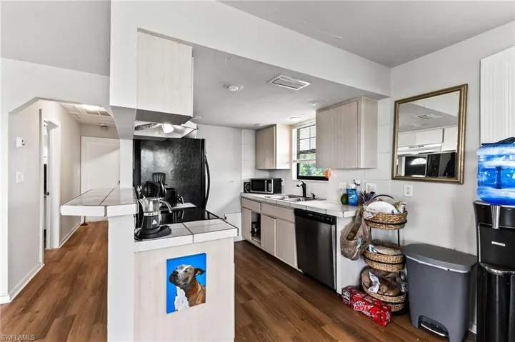 Kitchen with dark wood-type flooring, tile counters, appliances with stainless steel finishes, and sink