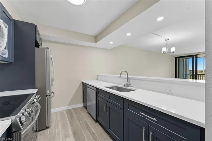 Kitchen featuring recessed lighting, stainless steel appliances, wood tiled floors, light stone counters, and hanging light fixtures