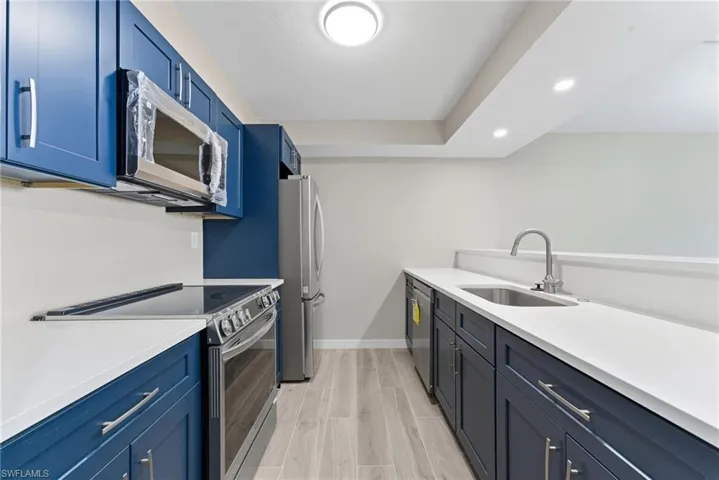 Kitchen featuring blue cabinetry, appliances with stainless steel finishes, recessed lighting, wood tiled floors, and light stone countertops