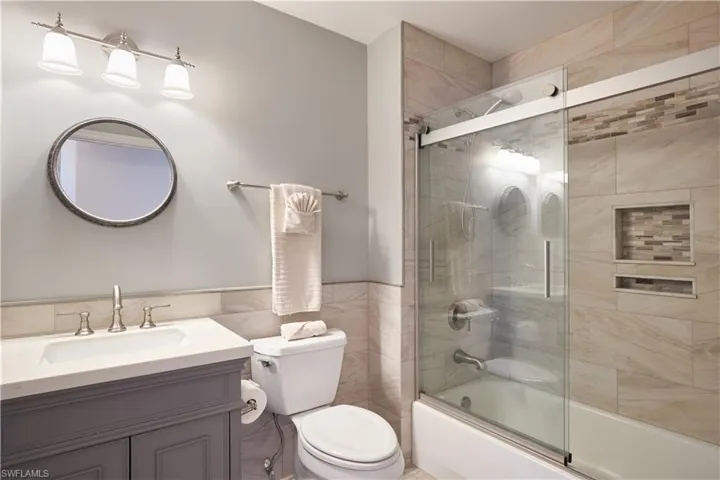 Full bathroom with vanity, enclosed tub / shower combo, tile walls, and toilet
