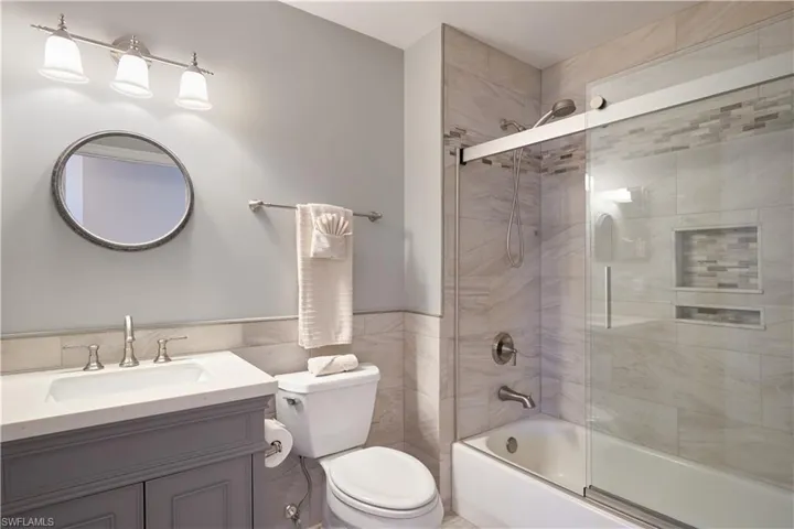 Full bathroom featuring vanity, toilet, shower / bath combination with glass door, and tile walls