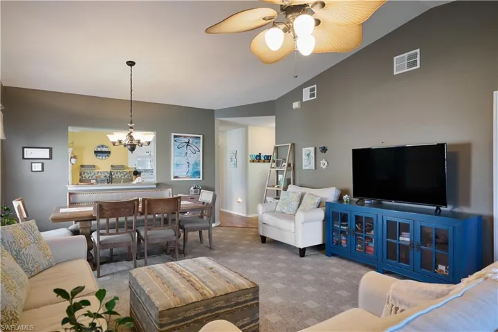 Carpeted living room with ceiling fan with notable chandelier and vaulted ceiling