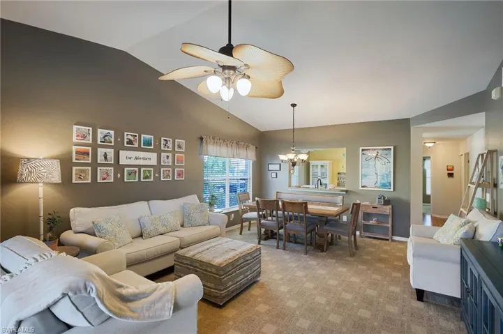 Living room with ceiling fan with notable chandelier, lofted ceiling, and light carpet