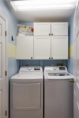 Clothes washing area featuring washing machine and clothes dryer and cabinets
