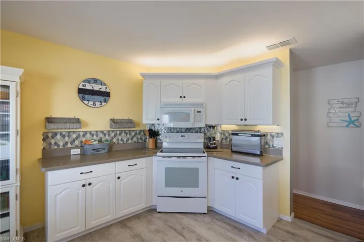 Kitchen with backsplash, light hardwood / wood-style flooring, white cabinets, and white appliances