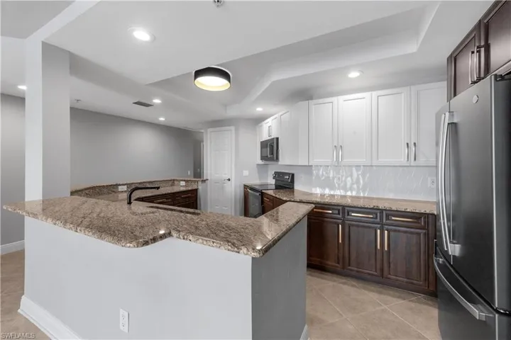 Kitchen featuring appliances with stainless steel finishes, white cabinetry, light tile patterned floors, and kitchen peninsula