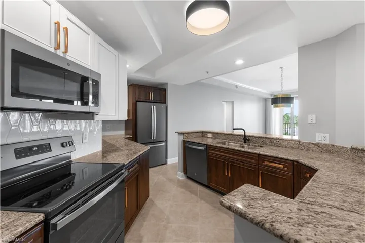 Kitchen featuring light tile patterned flooring, a tray ceiling, stainless steel appliances, white cabinets, and sink