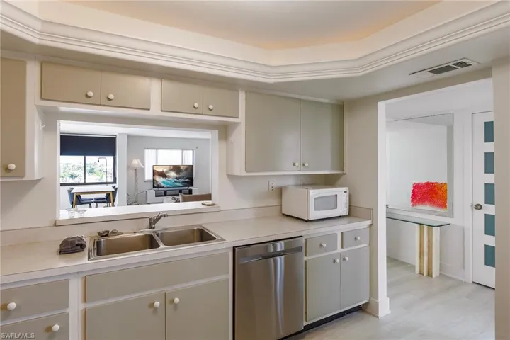 Kitchen featuring stainless steel dishwasher, light countertops, white microwave, and light wood-style floors