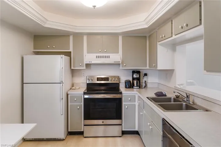 Kitchen with appliances with stainless steel finishes, light countertops, extractor fan, and a raised ceiling