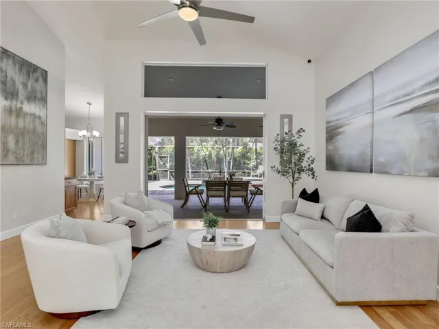 Living room featuring light wood-type flooring, french doors, ceiling fan with notable chandelier, and vaulted ceiling