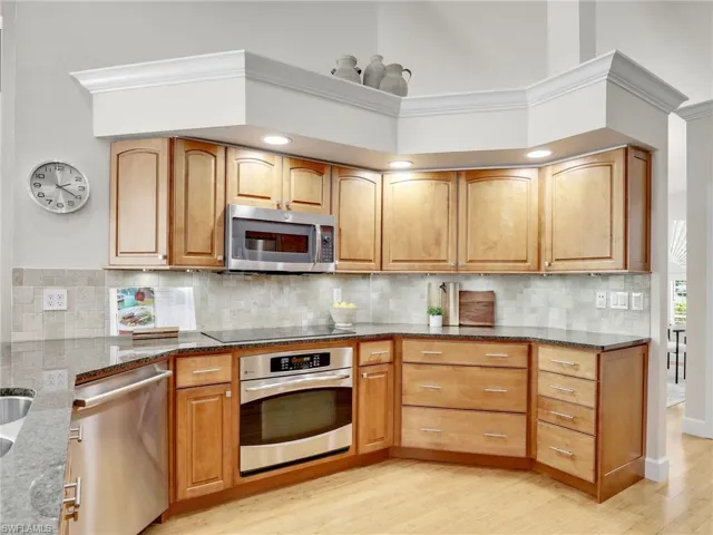 Kitchen with ceiling fan with notable chandelier, stone counters, stainless steel fridge, light wood-type flooring, and tasteful backsplash