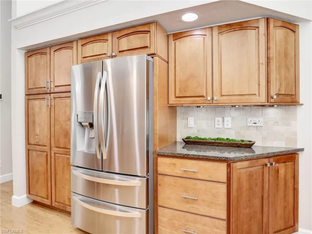 Kitchen featuring appliances with stainless steel finishes, dark stone counters, light hardwood / wood-style flooring, decorative backsplash, and a high ceiling