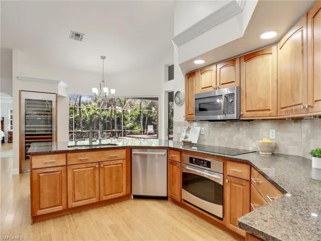 Kitchen with decorative backsplash, light hardwood / wood-style flooring, stainless steel refrigerator with ice dispenser, and dark stone countertops
