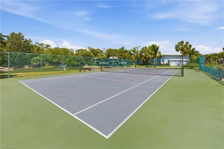 Outdoor tennis court featuring a gray playing surface with white and red lines, green perimeter, and a black net