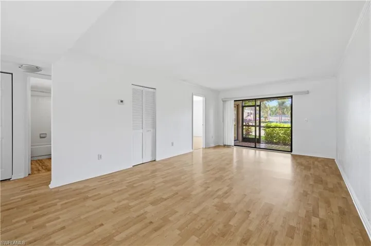 Expansive room featuring light wood-finish flooring and a large sliding glass door opening to outdoor greenery