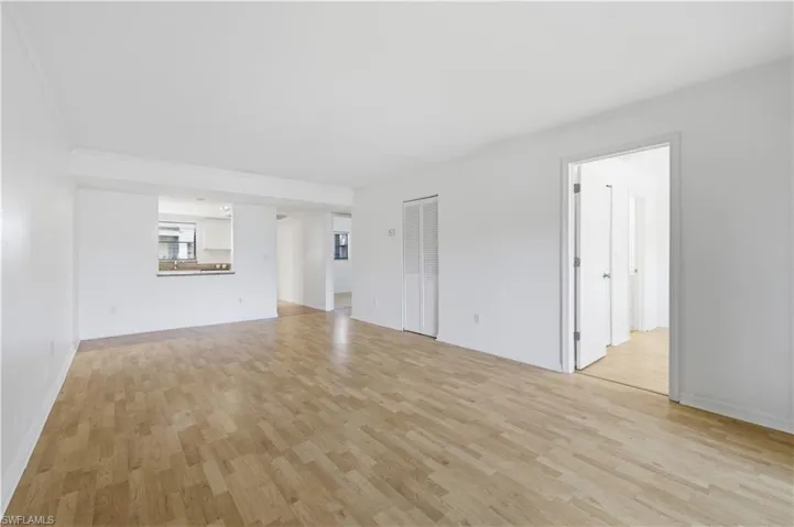 Bright interior space featuring wood-finish flooring, white painted walls, and a pass-through window to an adjacent room