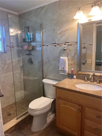 Master Bathroom with a tile shower, tile walls, vanity, toilet, and crown molding