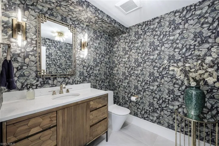1/2 Bathroom with wallpapered walls, vanity, and light tile patterned floors