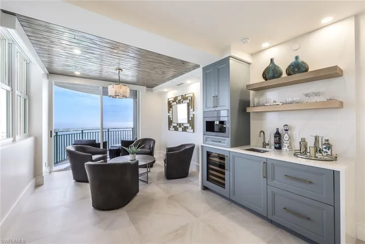 Indoor wet bar with open shelves, gray cabinets, light stone counters, wine cooler, and hanging light fixtures