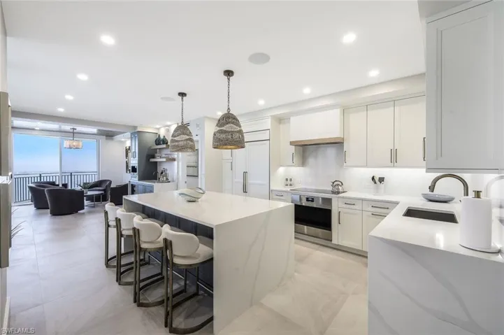 Kitchen with light stone counters, a kitchen bar, a center island, oven, and hanging light fixtures