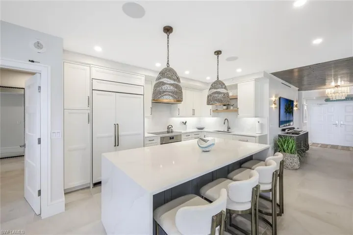 Kitchen featuring white cabinetry, decorative light fixtures, paneled refrigerator, a breakfast bar, and light stone countertops