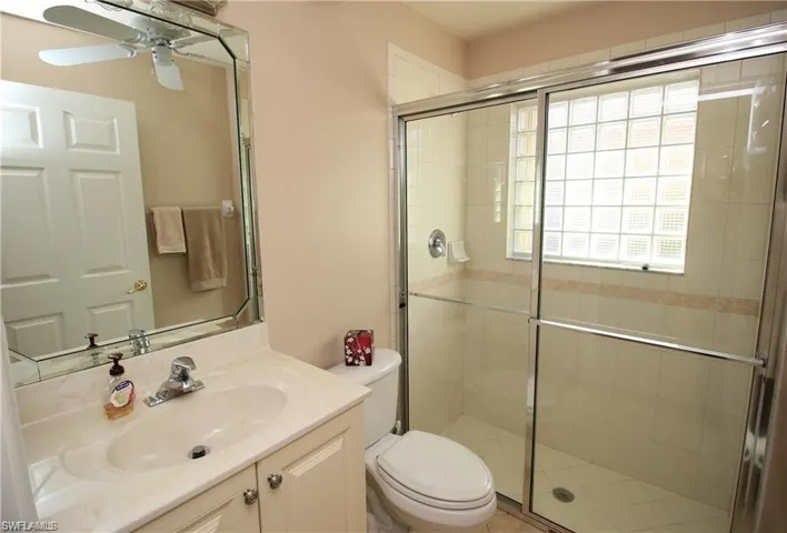 Bathroom with walk in shower, toilet, ceiling fan, and vanity