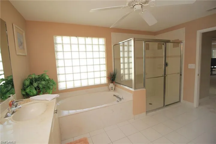 Bathroom with tile patterned flooring, vanity, ceiling fan, and plus walk in shower