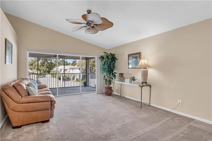 Living room with light carpet, lofted ceiling, and ceiling fan with sliders to lanai