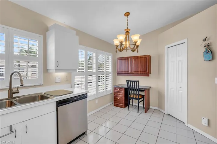 Kitchen featuring stainless steel dishwasher, sink, decorative light fixtures, built in desk area, pantry and a wealth of natural light