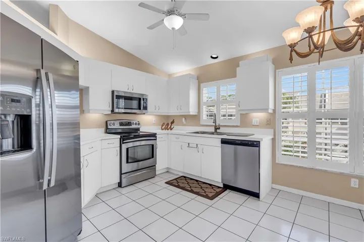 Kitchen with appliances with stainless steel finishes, sink, lofted ceiling, decorative light fixtures, and white cabinets