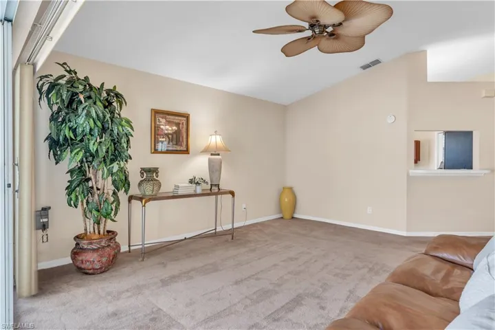 Living room with light carpet, lofted ceiling, and ceiling fan with sliders to lanai