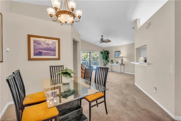 Carpeted dining room with vaulted ceiling and ceiling fan with notable chandelier