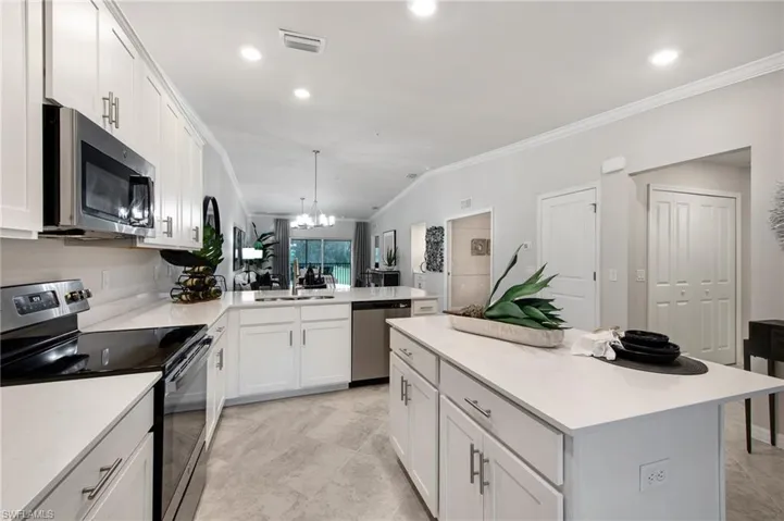 Kitchen with stainless steel appliances, hanging lights, white cabinets, and crown molding