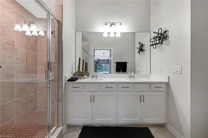 Full bath with a stall shower, double vanity, and light tile patterned floors