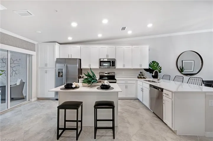 Kitchen featuring a breakfast bar, white cabinets, vaulted ceiling, crown molding, and stainless steel appliances