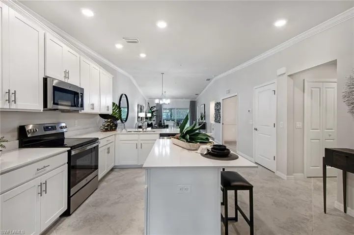 Kitchen featuring stainless steel appliances, crown molding, white cabinets, a breakfast bar, and hanging lights
