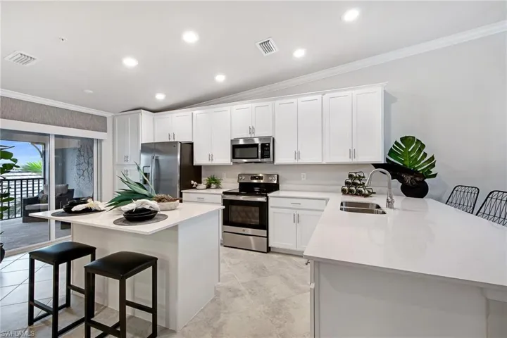Kitchen with a breakfast bar, stainless steel appliances, vaulted ceiling, crown molding, and white cabinets