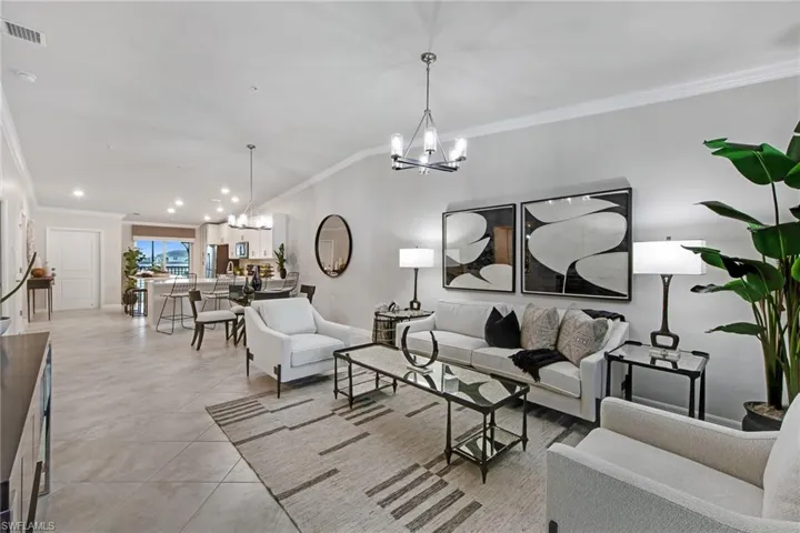 Living room featuring crown molding, a chandelier, lofted ceiling, and light tile patterned floors
