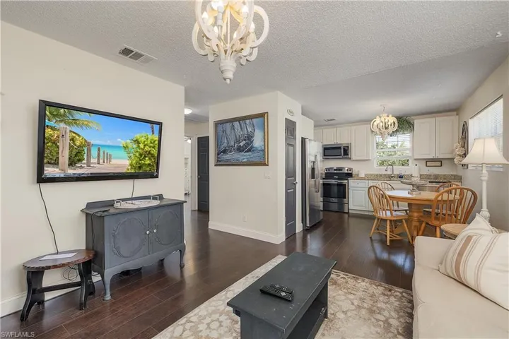 Living room with a notable chandelier, dark laminate / wood-style flooring, and a textured ceiling