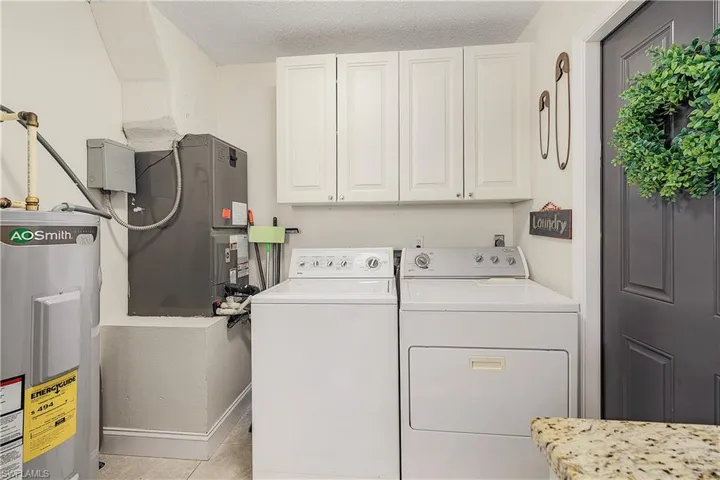 Clothes washing area with cabinets, light tile flooring, separate washer and dryer, a textured ceiling, and electric water heater