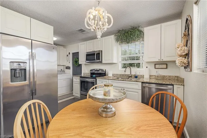 Kitchen featuring an inviting chandelier, sink, washer / clothes dryer, white cabinetry, and appliances with stainless steel finishes